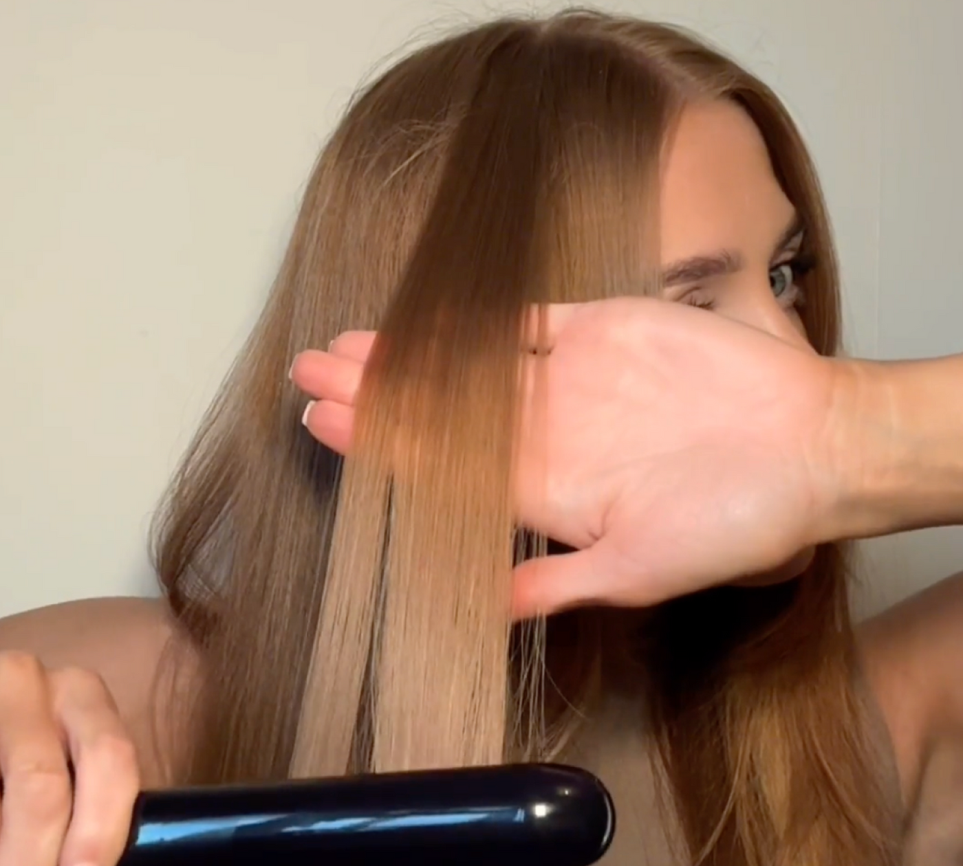 Woman using the KEEO Smart Glide Straightener to style her hair, revealing a visibly smoother, shinier section compared to untreated strands.