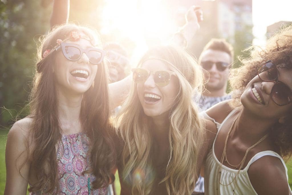 Three friends laughing together outdoors with sunglasses on