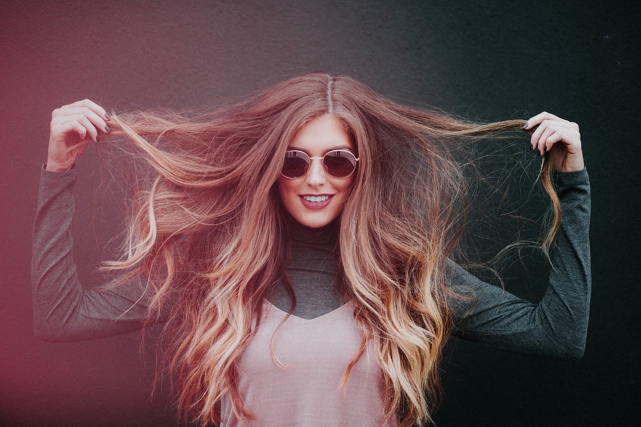 Woman with long, wavy hair holding it in front of a dark background