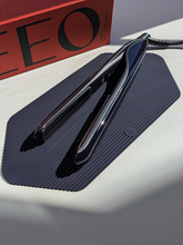 Black hair straightener on a textured black mat with a red box in the background