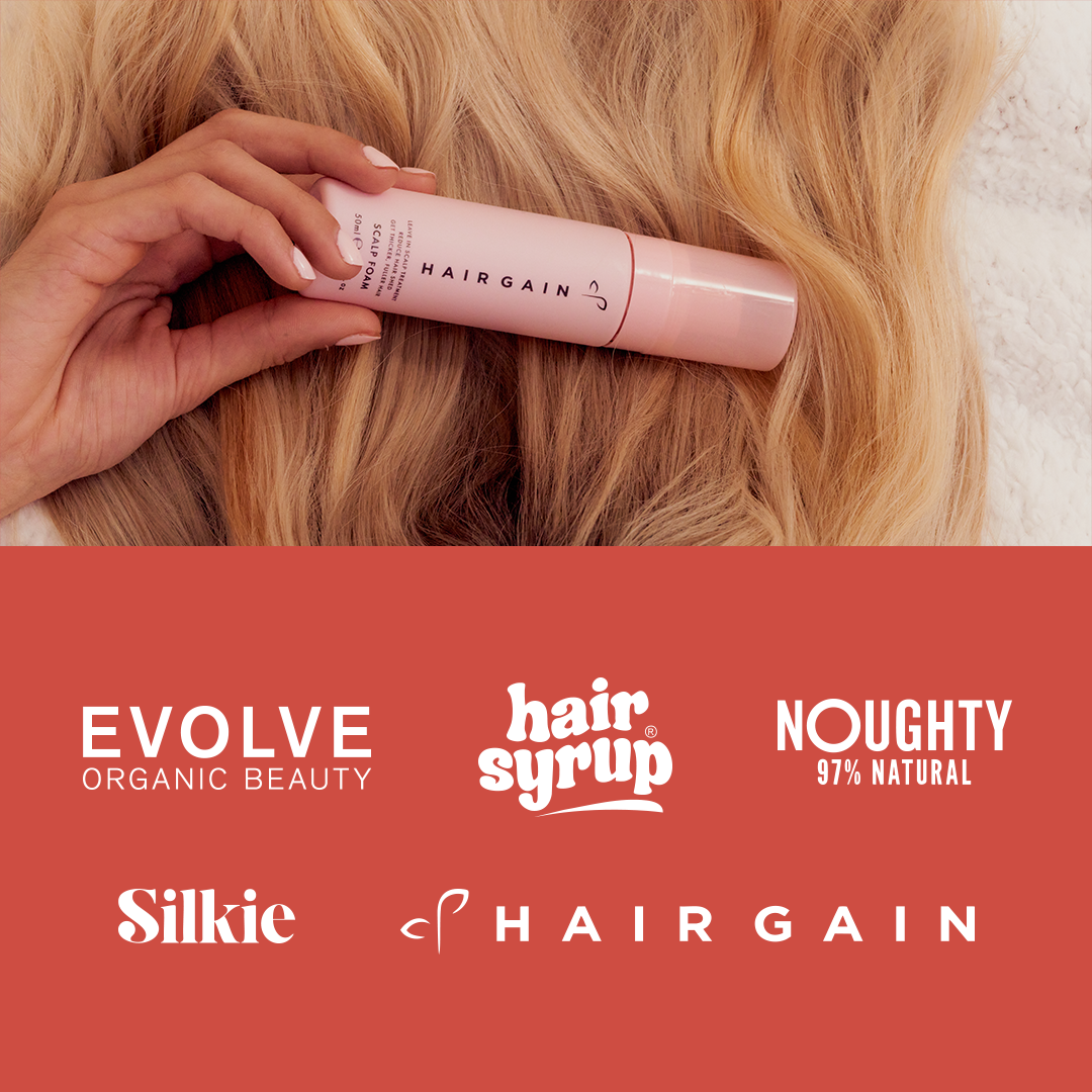 Hand holding a bottle of Hairgain product with visible brand logos at the bottom.