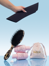 Silkie hair care products including a brush, bottles, and a pouch on a light blue background