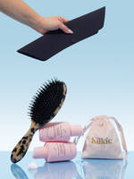 Silkie hair care products including a brush, bottles, and a pouch on a light blue background